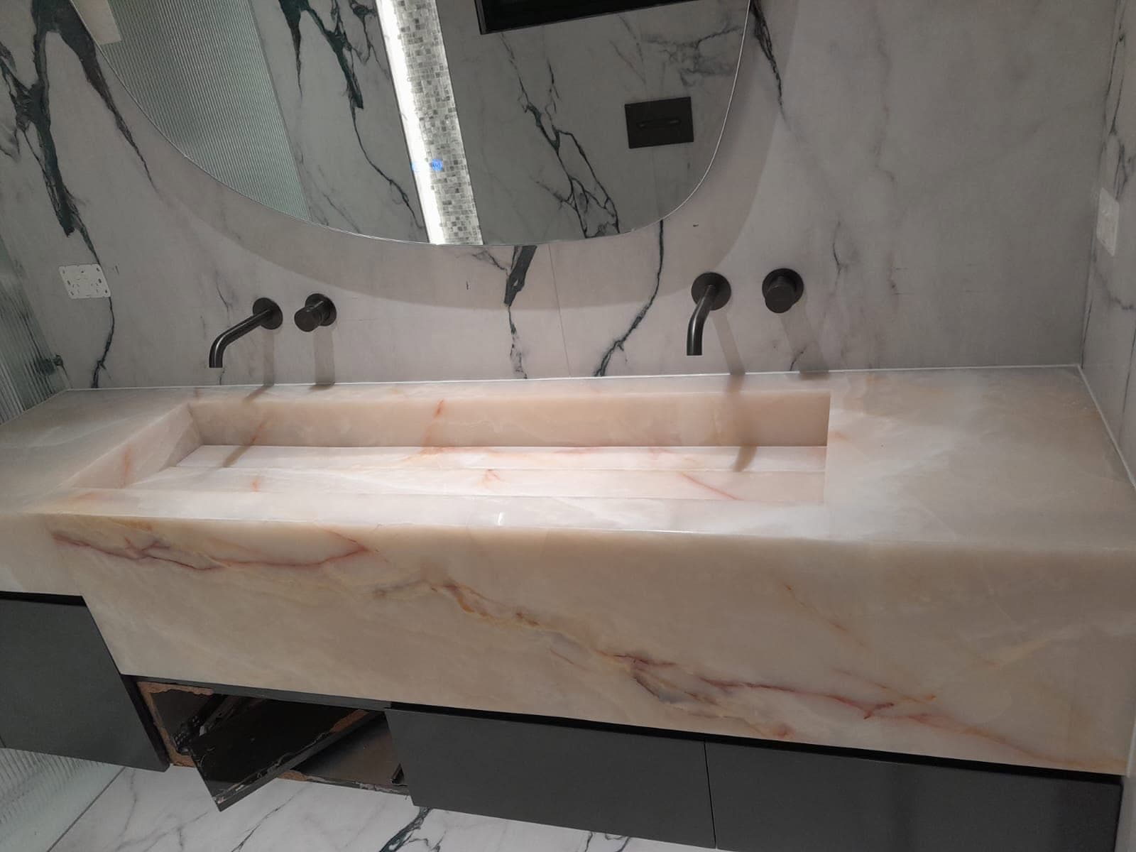 Translucent pink onyx vanity with an integrated trough basin and a book-matched onyx wall