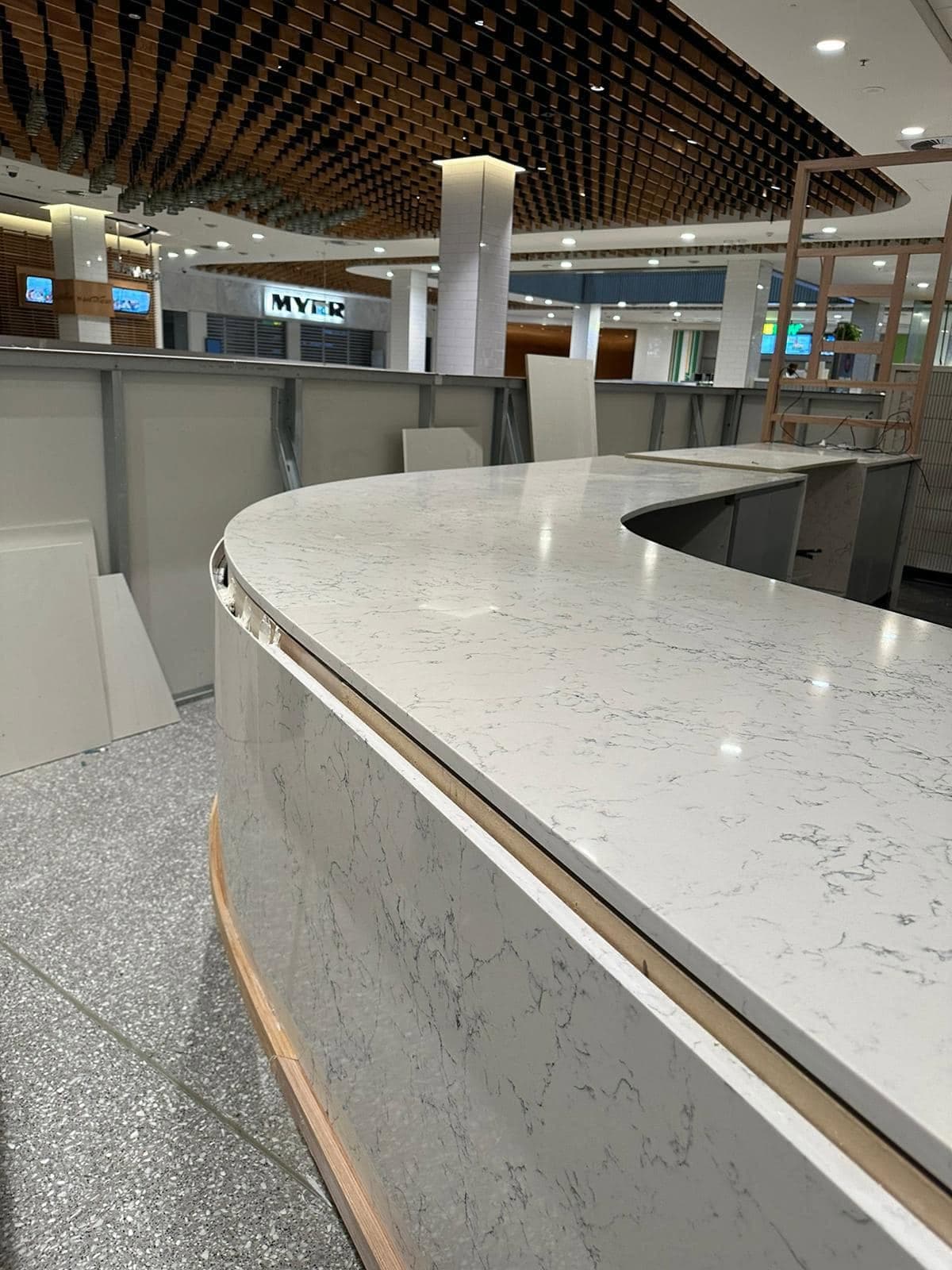Serpentine white marble-look retail counter under a timber-batten ceiling in a shopping centre