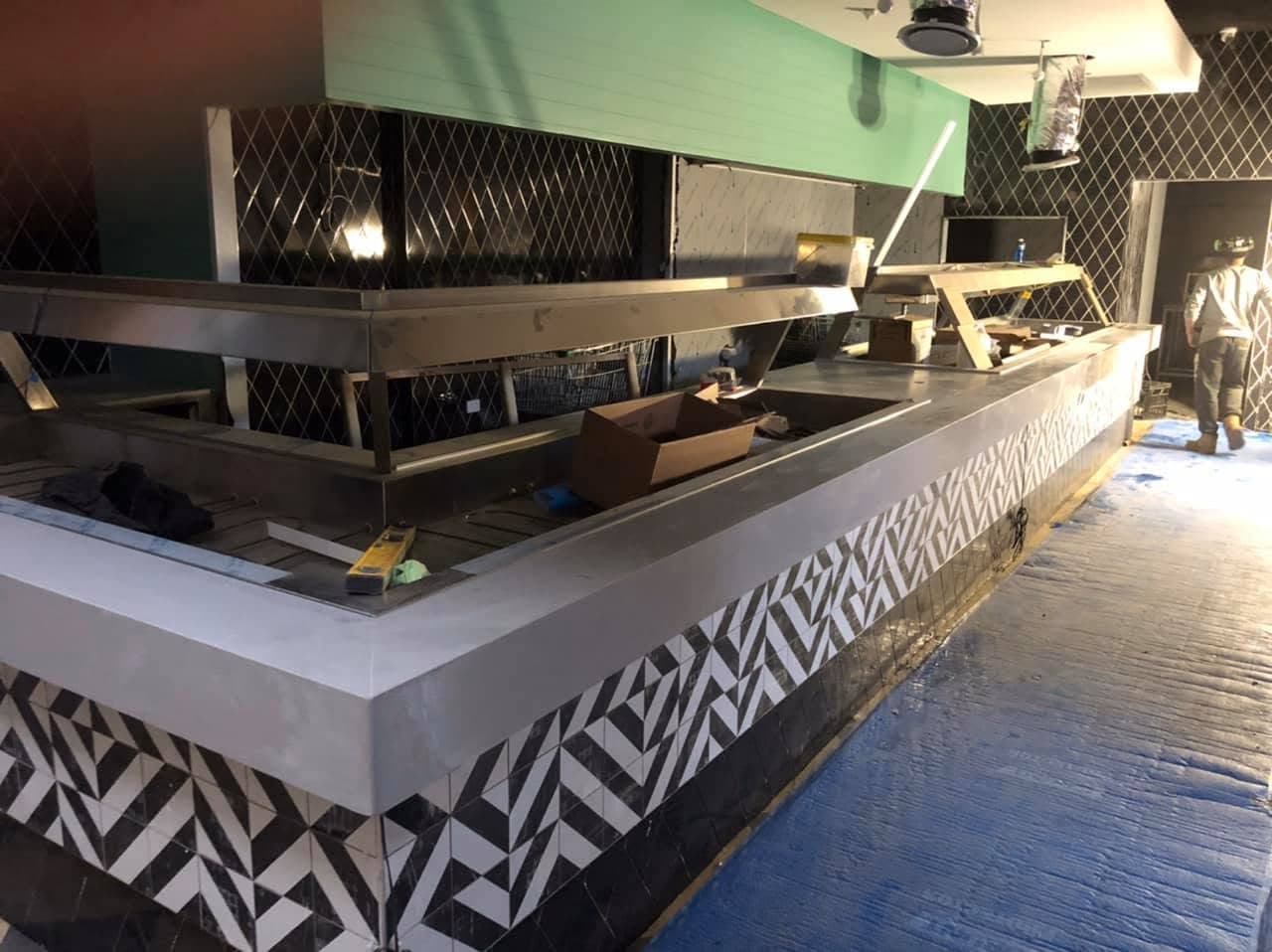 Stainless and stone servery counter with a geometric black and white tiled front, mid fit-out