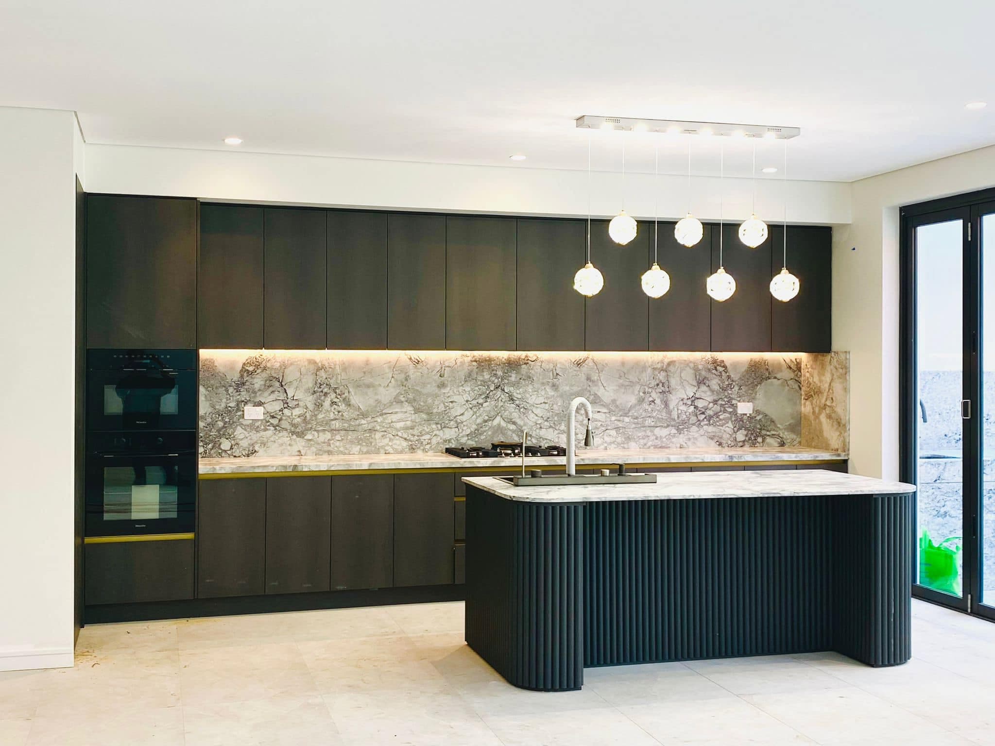 Black fluted curved island with brass trims and a full-height grey and brown veined splashback