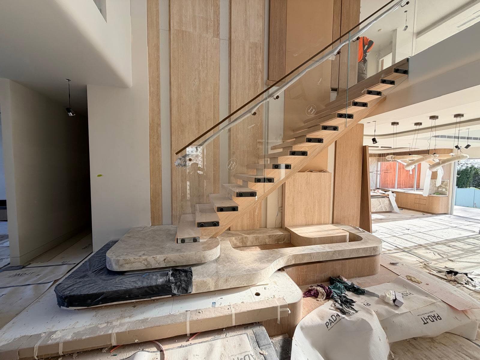 Travertine-clad floating staircase with a curved base slab and frameless glass balustrade