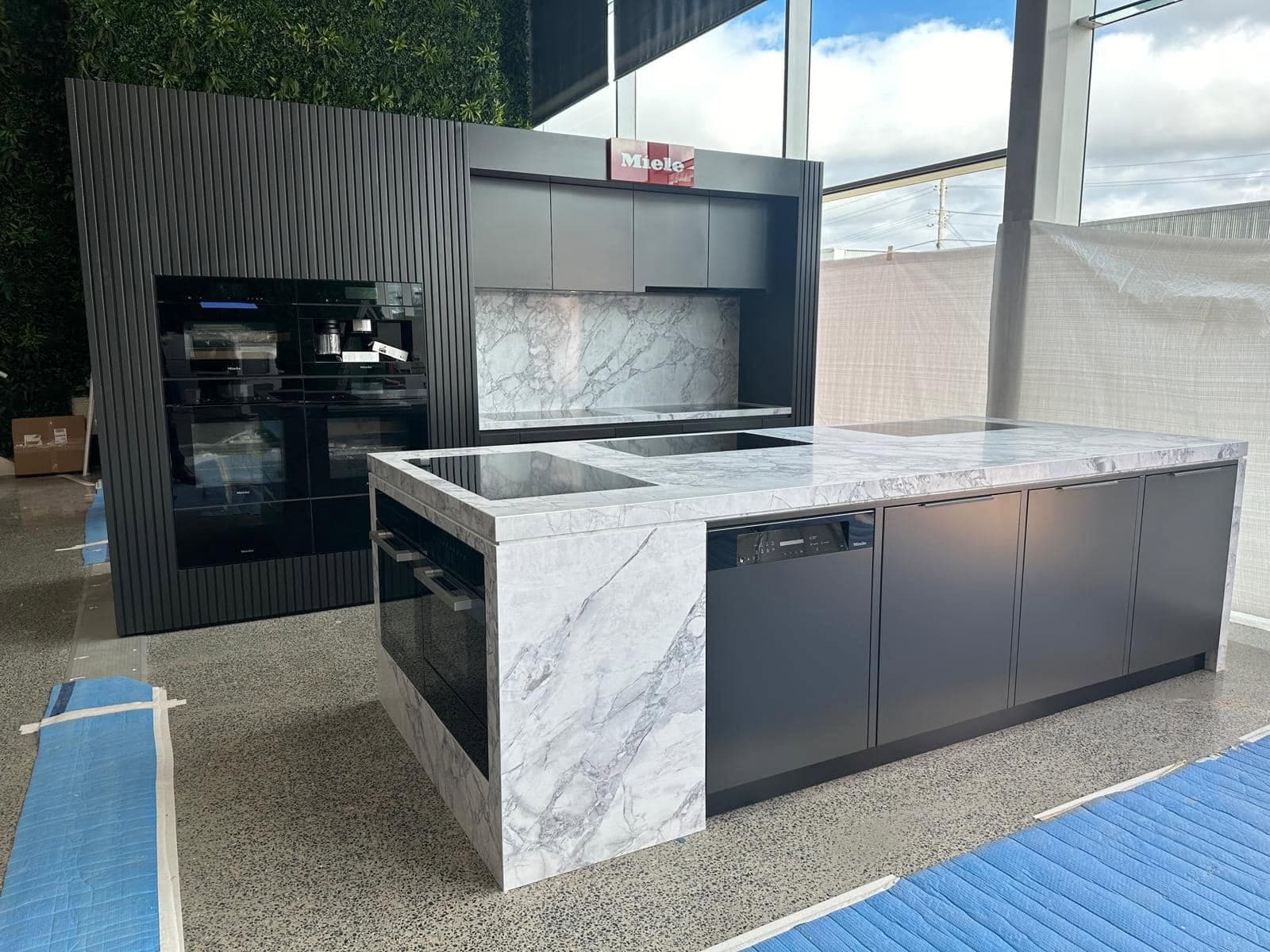 Showroom island with a Calacatta-look benchtop and waterfall ends beside a Miele appliance wall