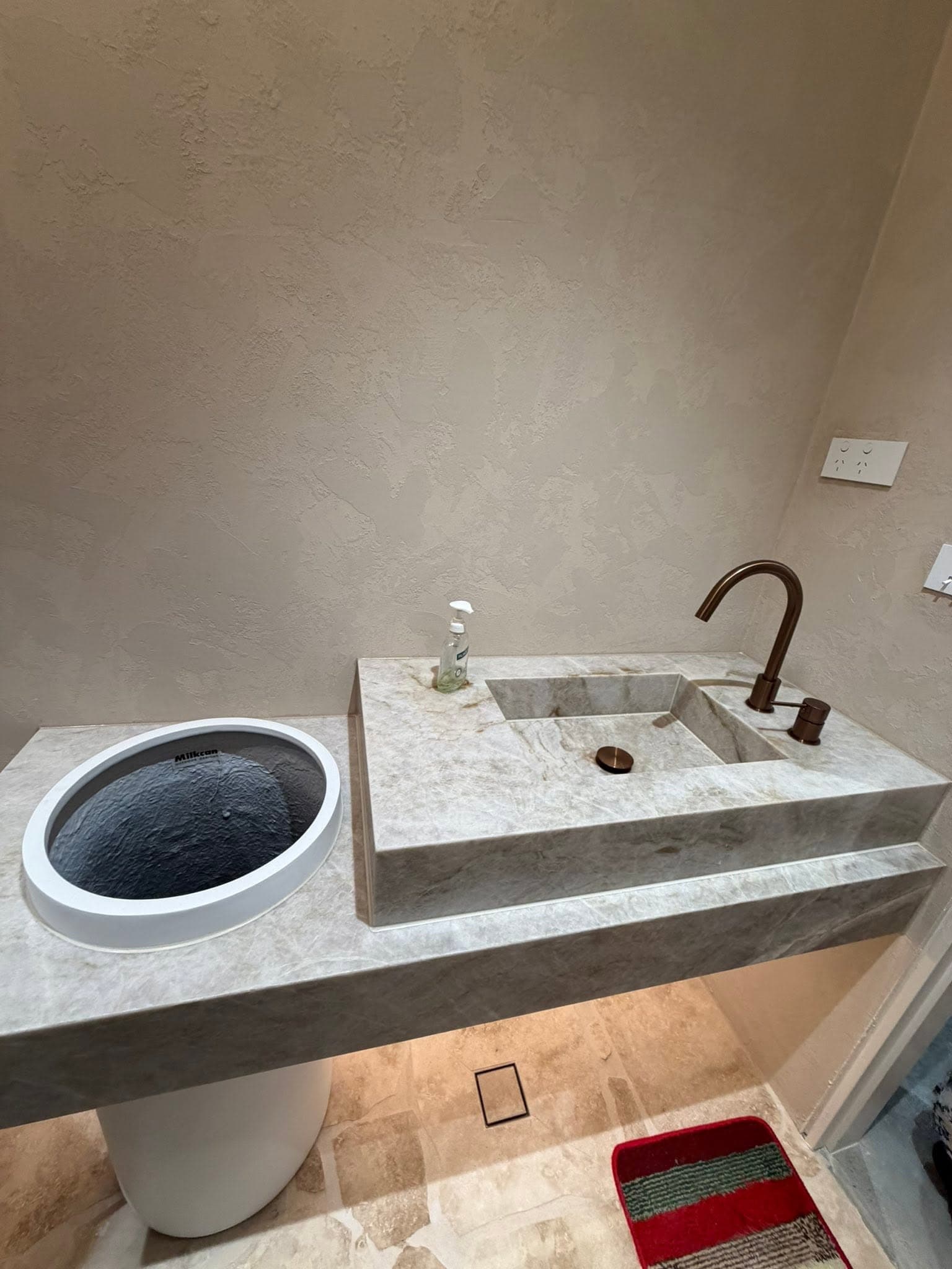 Floating stone vanity with an integrated carved basin and bronze tapware in a powder room