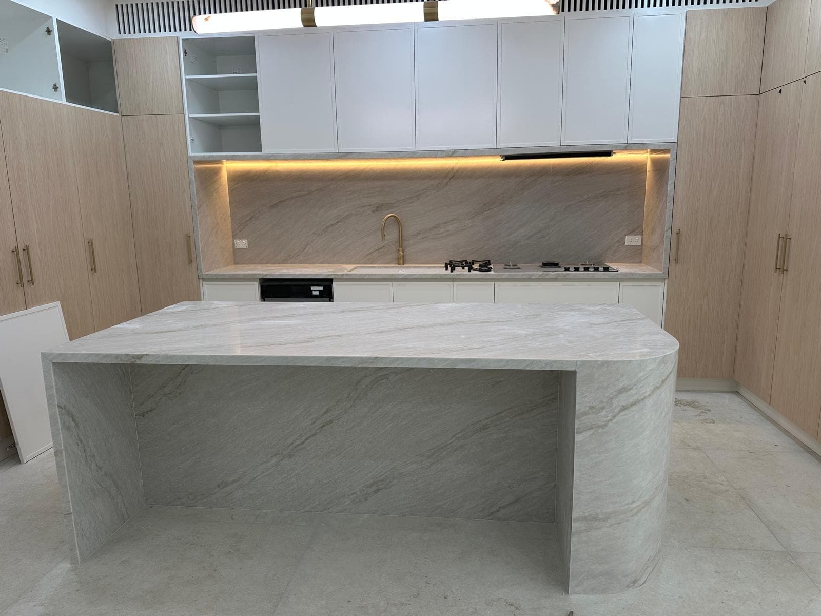 Grey and beige marble-look island with a curved end and an open sculpted leg, brass tap