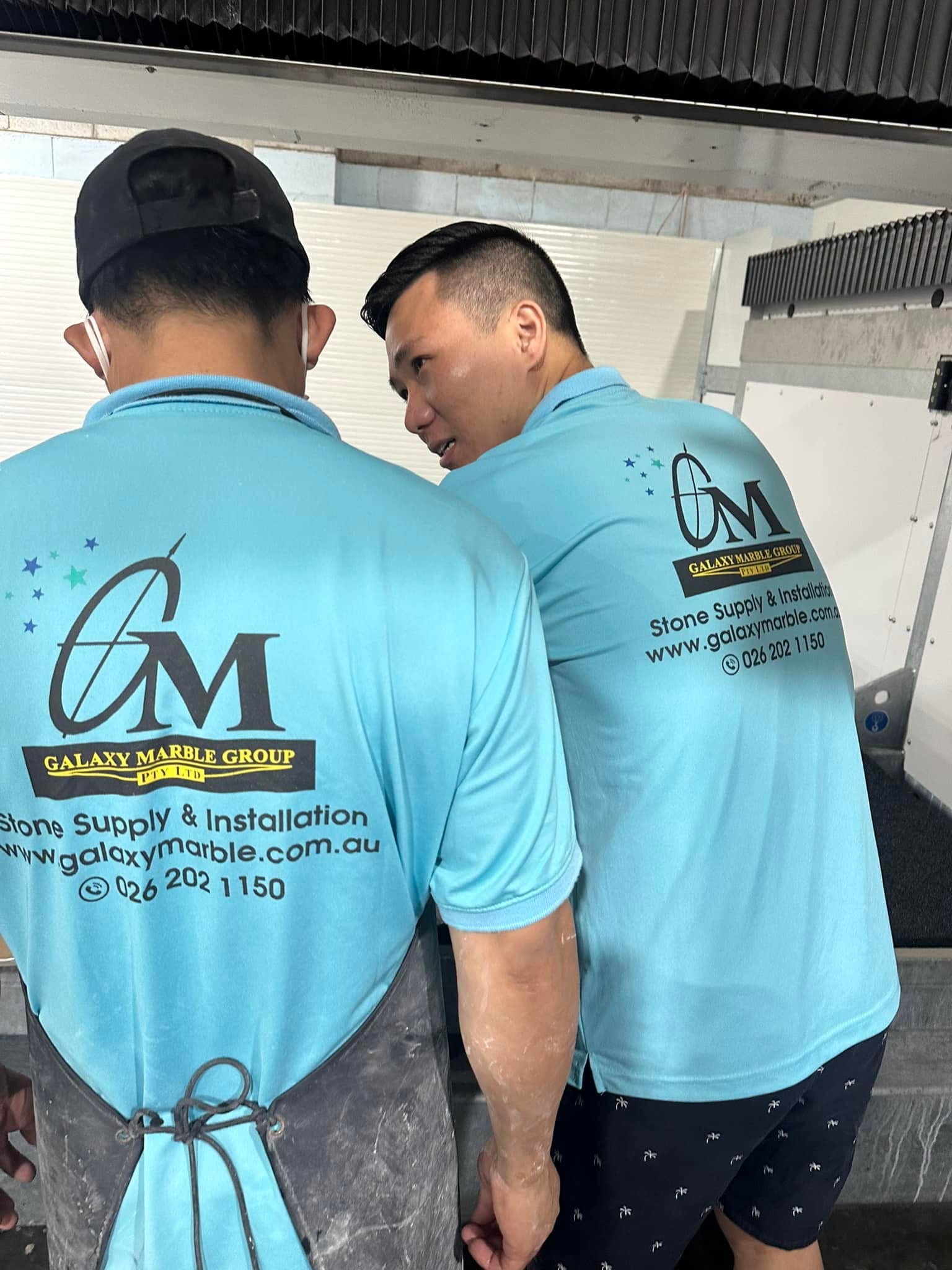 Two Galaxy Marble Group fabricators in branded uniform at the workshop saw
